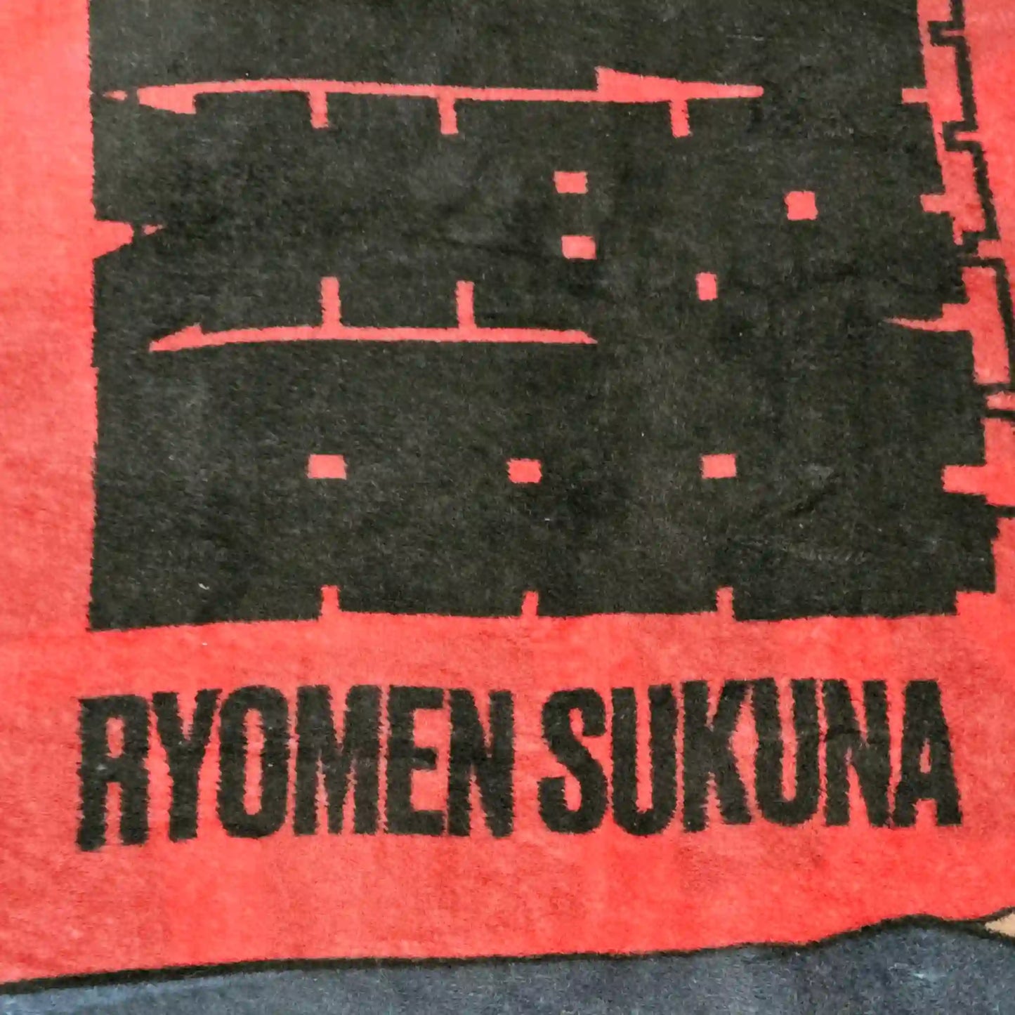 Detalle de texto “Ryomen Sukuna” en cobija de Jujutsu Kaisen con letras negras sobre fondo rojo.