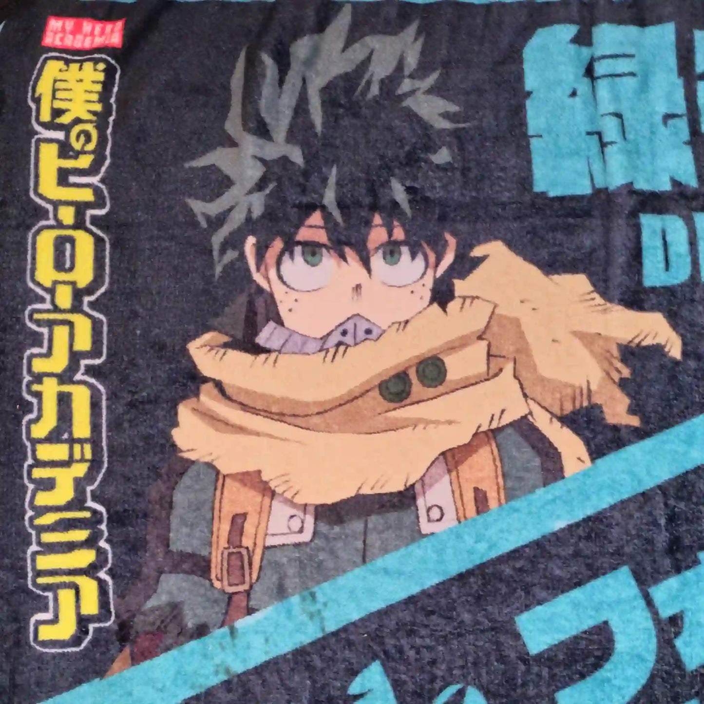Primer plano del rostro de Deku en cobija de My Hero Academia con detalles en amarillo y negro