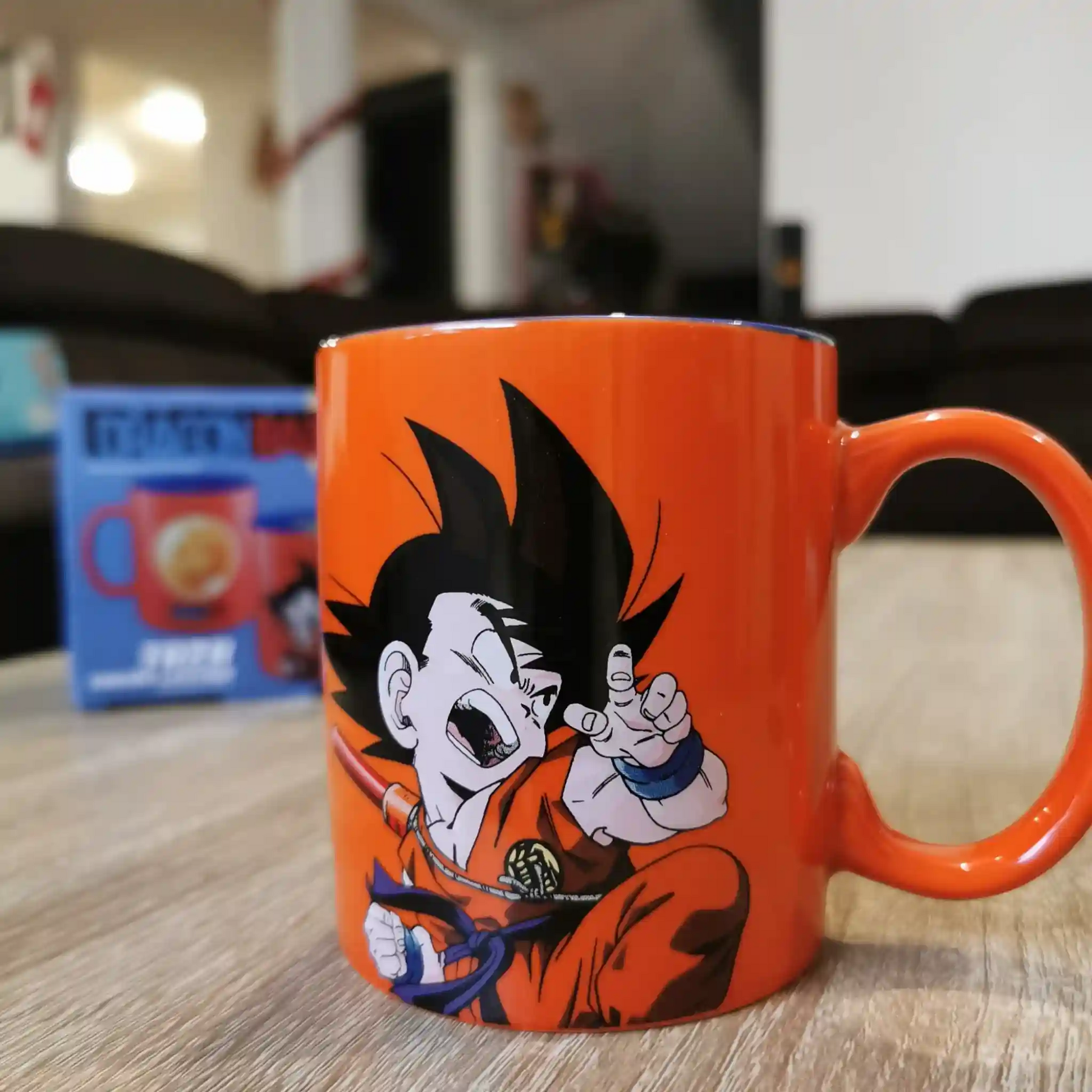Taza de Dragon Ball con diseño de Goku niño en posición de combate, sobre una mesa con su empaque al fondo